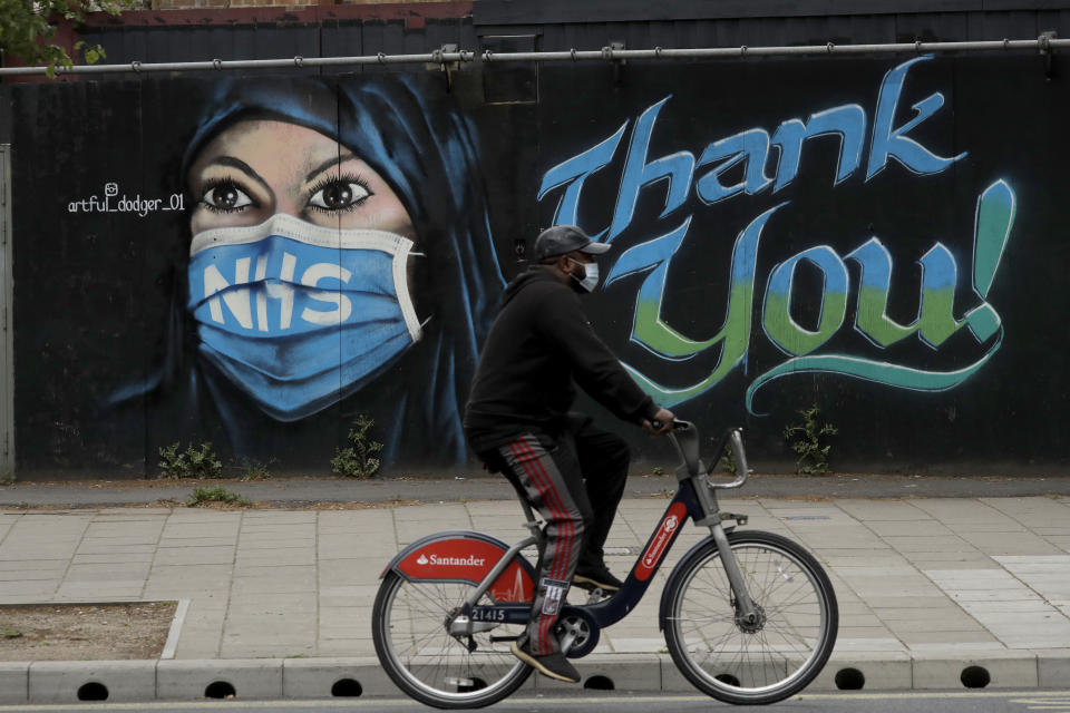 A man wearing a face mask cycles past a recently painted piece of street art by The Artful Dodger (A. Dee) entitled 'NHS Dedication Mural', thanking national health service workers, during the coronavirus lockdown in the Elephant and Castle area of London, Sunday, May 3, 2020. The highly contagious COVID-19 coronavirus has impacted on nations around the globe, many imposing self isolation and exercising social distancing when people move from their homes. (AP Photo/Matt Dunham)