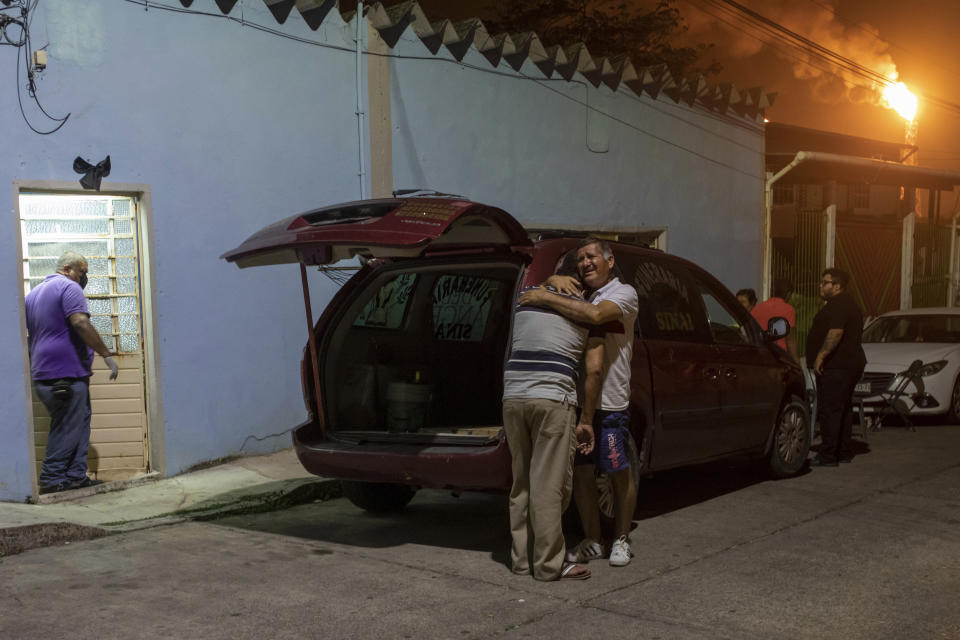 Artemio García, padre de la videoperiodista Sheila Johana García Olivera, de espaldas a la cámara, es abrazado por uno de sus hermanos después de sacar el ataúd de su hija del vehículo a la casa de la familia para su velatorio en Minatitlán en el estado de Veracruz, México, la madrugada del martes 10 de mayo de 2022. (AP Foto/Felix Marquez)