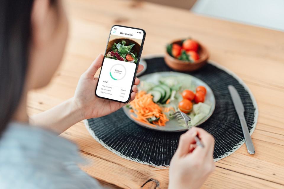 young woman using calorie counter app on smartphone while eating salad