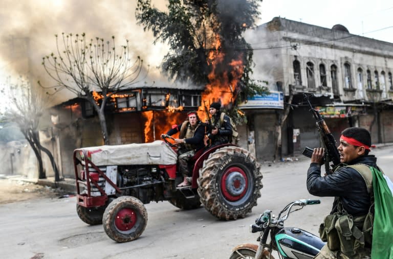 A Turkish-backed Syrian rebel drives past a burning shop in the city of Afrin in northern Syria on March 18, 2018