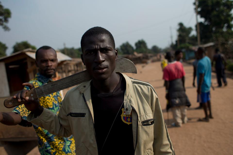 FILE - In this Tuesday, Dec. 31, 2013 file photo, a member of an armed neighborhood defense squad, which residents say is not anti-balaka, but local Christian residents protecting themselves, carries a machete as he walks near a roadblock in Bangui, Central African Republic. The body of a man said to be Muslim lay nearby. Central African Republic has long teetered on the brink of anarchy, but the new unrest unleashed by a March 2013 coup has ignited previously unseen sectarian hatred between Christians and Muslims. More than 1,000 people were killed in December alone and nearly 1 million displaced. The crisis has forced some to flee across borders to desperately poor and unstable countries like Chad and Congo. (AP Photo/Rebecca Blackwell, File)