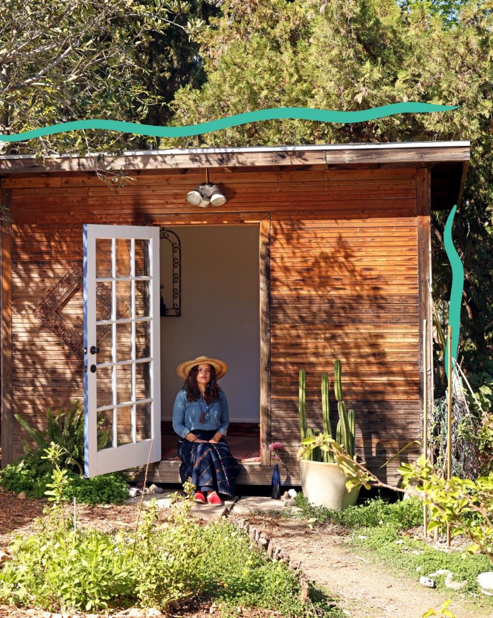 A woman sits in the open doorway of a small wooden building.