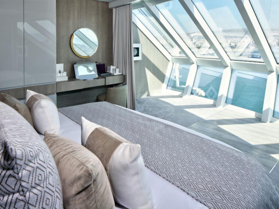 a bed facing windows looking out into the ocean with a makeup vanity next to the bed