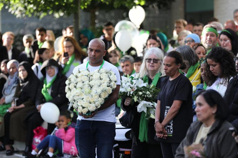 Babies were the only ones heard crying; the tears of the rest fell silently.The procession of families and residents, memories of tragedy fresh again in their minds, wound its way through eerily noiseless streets closed to traffic. The huge crowd of people of all ages and backgrounds had gathered to mark the second anniversary of the Grenfell Tower fire. Young people who in other circumstances might have been too cool to join a march walked alongside parents and grandparents for the silent vigil that began and ended in the shadow of the tower in west London.They came to show solidarity, to support and comfort one another in their grief and to fight for the right of others not to die in an inferno like that on 14 June 2017, that killed 72 people.They were joined by Benjamin Zephaniah, the poet and playwright, and rapper Stormzy, who walked among the crowd of thousands, almost all of whom wore green and many of whom carried placards calling for justice.Lowkey, a rapper, addressed the crowd and said the fire should be a “never-again moment”. He added that the government should more strongly regulate building firms “before we regulate you”.Earlier, James Brokenshire, the communities secretary, and Sadiq Khan, the London mayor, had laid flowers alongside bereaved relatives at a private ceremony yards from the burnt-out buildingA 72-second silence, one second representing each victim, was held before the names of the dead were read aloud.Residents joined a multi-faith vigil and a mass to pray no such disaster would happen again.Pastor Derrick Wilson of the Tabernacle Christian Centre said people were “anxious for justice”, as he led prayers.Two years exactly since the fire that exposed a deep social divide at the heart of one of London’s wealthiest boroughs, they spoke again of authorities dragging their feet and of the dangers of flammable cladding.According to new government figures, 24,800 homes in 272 buildings are still covered in highly flammable material similar to that used on Grenfell Tower. The Independent has found almost 60,000 people are still living in tower blocks with such cladding.The blaze is still a source of anger, with many local residents accusing the authorities of racism against the largely ethnic-minority occupants of Grenfell Tower.Stephanie Vaz, a wheelchair-user who lives close by, said she still gets panic attacks whenever the fire alarm at her home goes off.The anniversary events, she said, were about friends and families in the area giving each other strength and support. “Just seeing everyone together like this makes you want to fight more against the dangerous cladding on other buildings,” she said.“Coming together triggers memories – it’s something very special and it’s healing to be together.”On Thursday, survivors and victims’ relatives beamed fire safety warnings onto high-rise blocks of flats in London, Newcastle and Manchester, claiming the buildings were wrapped in dangerous cladding, not fitted with sprinklers, and had defective fire doors.The bereaved and other campaigners are disappointed that publication of the inquiry‘s first report on the disaster has been delayed until October, when it had been expected by now.The first phase of the inquiry looked at what happened on the night.Detectives investigating the fire say they have carried out 13 interviews under caution and that they expect to conduct more.