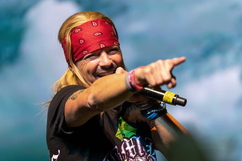 A man wearing a bandana holds a microphone and points his finger