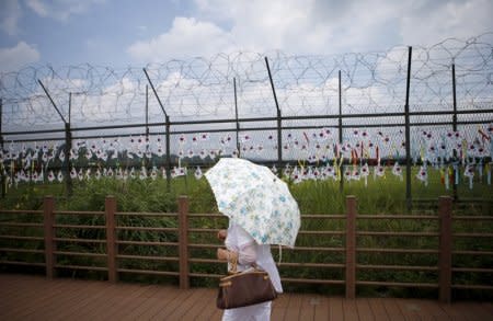 FILE PHOTO: A tourist holding a parasol walks by a barbed-wire fence decorated by South Korean national flags at the Imjingak pavilion near the demilitarized zone separating the two Koreas in Paju, South Korea, August 22, 2015.  REUTERS/Kim Hong-Ji/File Photo