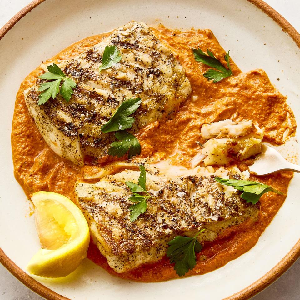 grilled cod on top of a spread of romesco sauce on a white plate topped with herbs