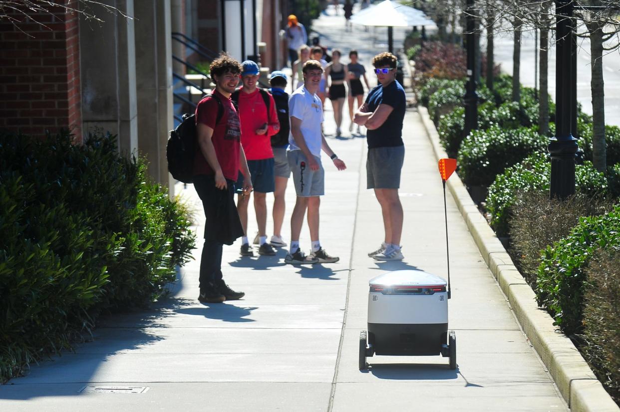 University of Tennessee students watch as a Starship delivery robot approaches them on Volunteer Boulevard.