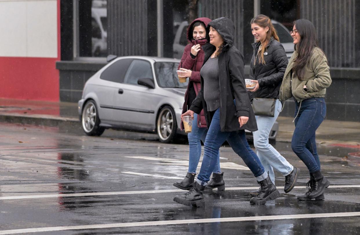 Maria Munoz, left, Marcela Gomez, Lynda Munoz, and Cintia Duarte walk along Main Street between Thursday's downpours in Visalia.