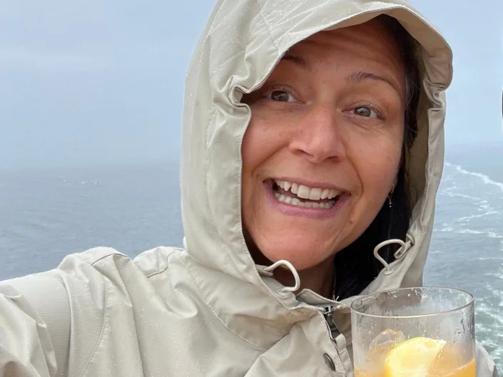 rebecca posing with a drink in her raincoat on an alaskan cruise