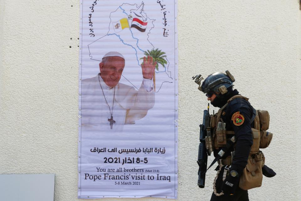 A security man walks near a poster of Pope Francis upon his upcoming visit to Iraq, in Baghdad (REUTERS)