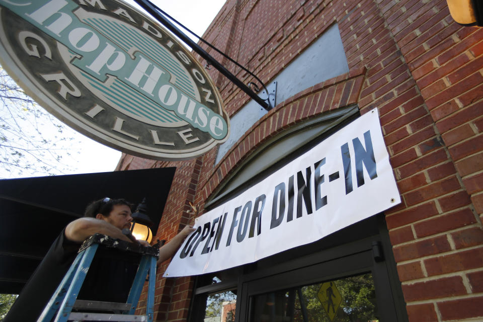 Jason Godbey hangs a banner over the entrance of Madison Chop House Grille on April 27, 2020, as they prepare to shift from take out only to dine-in service in Madison, Ga. (John Bazemore,/AP)