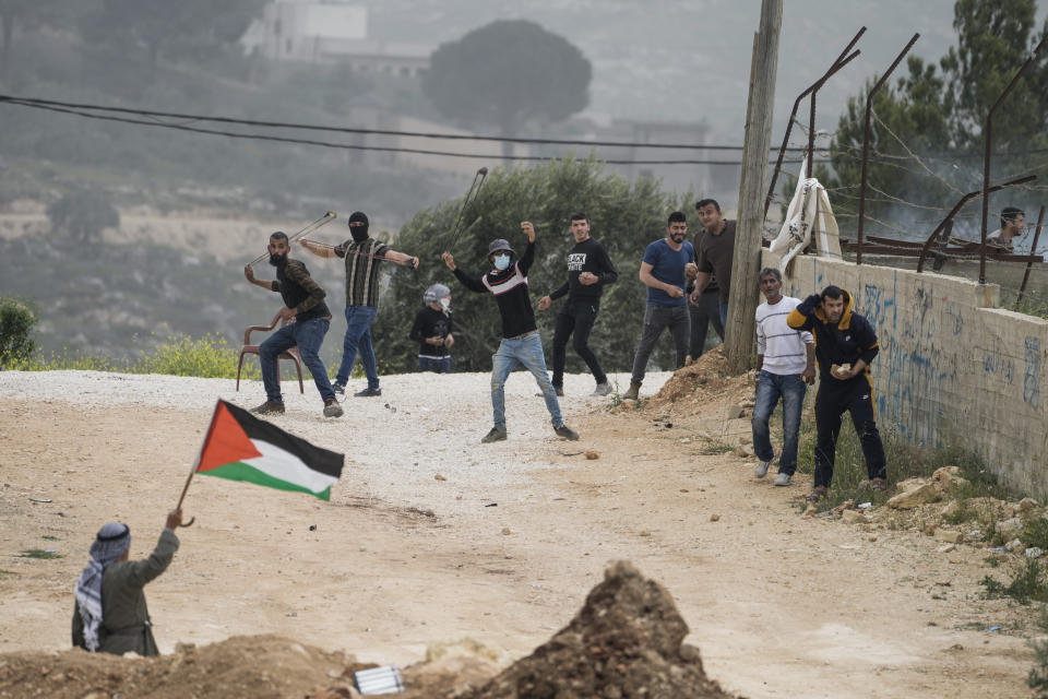 Palestinians hurl stones and wave a Palestinian flag toward Israeli soldiers to protest a march by Israeli settlers, in the West Bank village of Beita, Monday, April 10, 2023. Thousands of settlers marched to Eviatar, an unauthorized settlement outpost located next to Beita in the northern West Bank. (AP Photo/Majdi Mohammed)