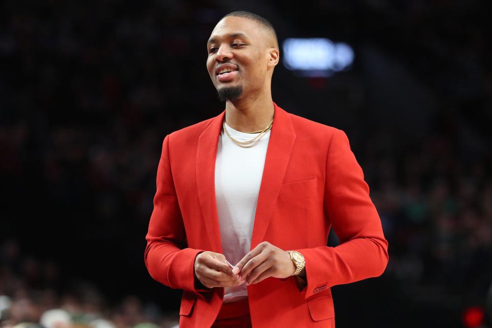 Damian Lillard pairs a red suit with a gold watch and gold chains.