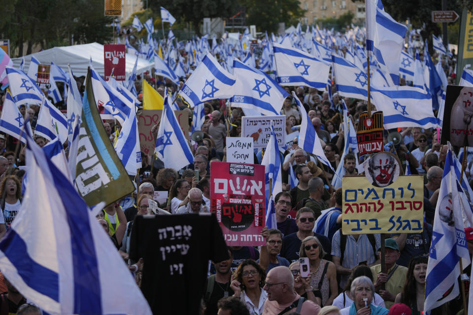 People wave Israeli flags during a protest against Israeli Prime Minister Benjamin Netanyahu's government, demanding new elections and the release of the hostages held in the Gaza Strip by the Hamas militant group, outside of the Knesset, Israel's parliament, in Jerusalem, Monday, June 17, 2024. The placard right reads:"Combat soldiers refuse to be killed because of Bibi." (AP Photo/Ohad Zwigenberg)