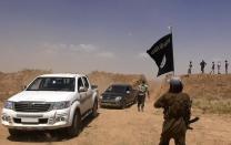 Image made available by the jihadist Twitter account Al-Baraka news on June 11, 2014 allegedly shows Islamic State militant waving the Islamic Jihad flag as vehicles drive on a newly cut road through the Syrian-Iraqi border