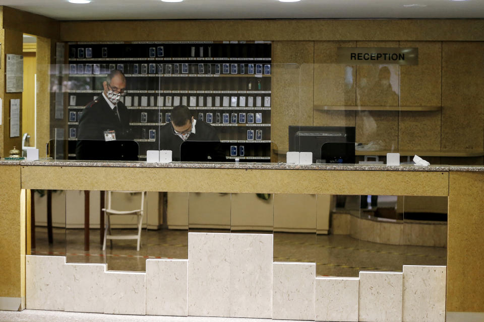 Two men wearing face masks to curb the spread of COVID-19 work in the reception of a hotel which hosts patients recovering from COVID-19 who need to undergo quarantine under the supervision of the Gemelli hospital, in Rome, Saturday, Nov. 14, 2020. (Cecilia Fabiano/LaPresse via AP)