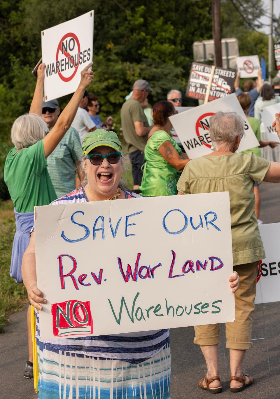 Sue Kozel shows her sign as she protests with several dozen people just outride Allentown. Protesters line Main St. just outside of Allentown where developers are proposing to build a warehouse and pave over a Revolutionary War site.