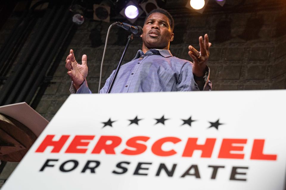 Herschel Walker, wearing a crisp blue shirt and no tie, at a podium marked: Herschel for Senate.