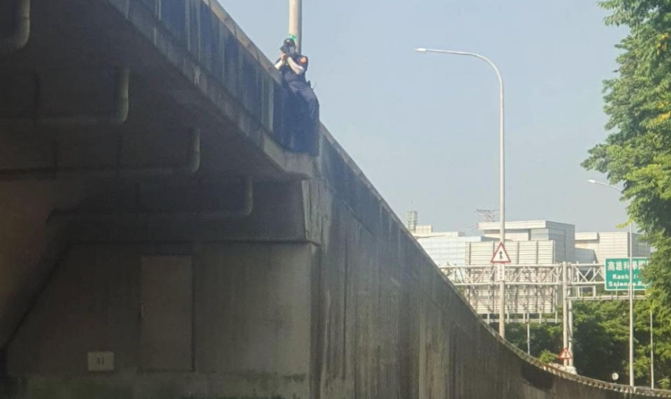 高雄科學園區匝道口前天有民眾赫見一名警員竟跨坐在1樓高的路肩護欄上，拿雷射測速槍在拍違規車輛，驚險景象直令人捏把冷汗！（圖片翻攝FB/記者爆料網）