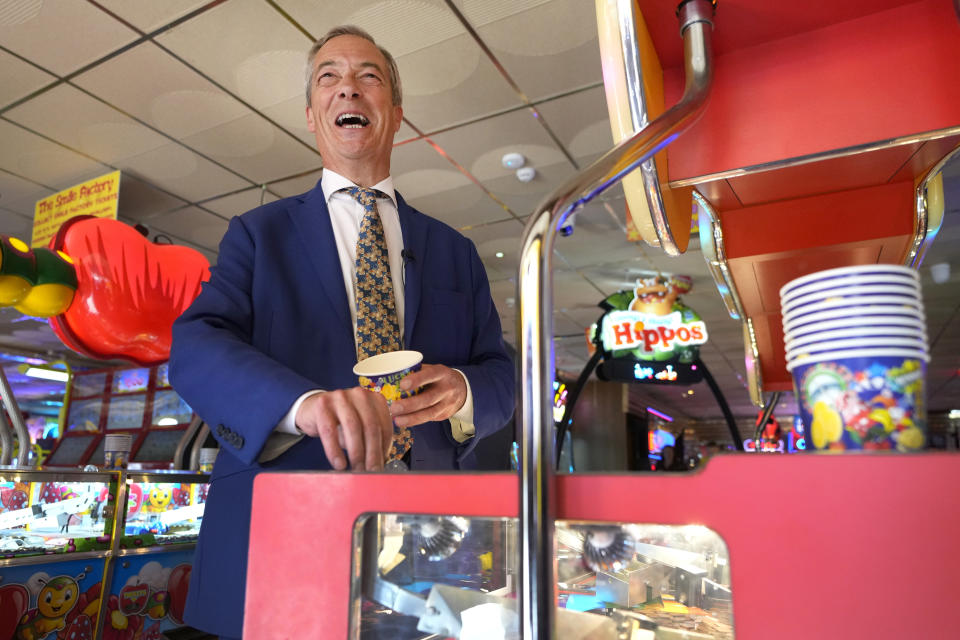 Britain's Nigel Farage, Reform UK party leader plays on a game in an amusement arcade holds out some coins whilst spending time with supporters in Clacton-On-Sea, Essex, England Friday, June 21, 2024. (AP Photo/Kirsty Wigglesworth)