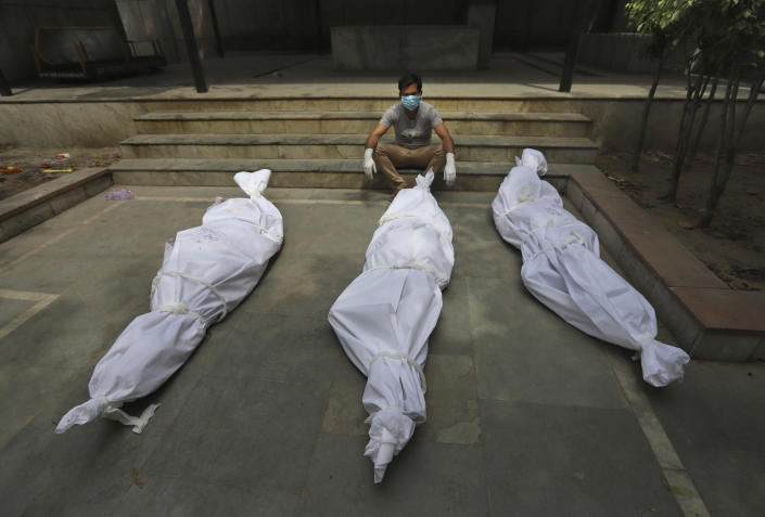 A man waits for the cremation of a relative who died of COVID-19, placed near bodies of other victims, in New Delhi, India, Tuesday, April 20, 2021. India has been overwhelmed by hundreds of thousands of new coronavirus cases daily, bringing pain, fear and agony to many lives as lockdowns have been placed in Delhi and other cities around the country. (AP Photo)