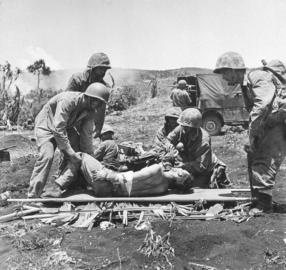 Marines tende to wounded comrades while the fighting rages on during the battle to take Saipan from the Japanese, 1944.