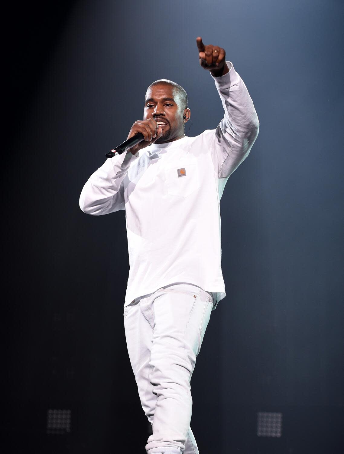 Man dressed in all white on a stage with a microphone