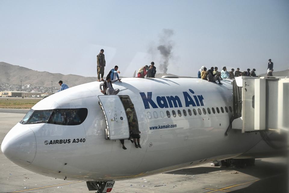 Afghan people climb atop a plane as they wait at the Kabul airport in Kabul on August 16, 2021, after a stunningly swift end to Afghanistan's 20-year war, as thousands of people mobbed the city's airport trying to flee the group's feared hardline brand of Islamist rule. (Photo by Wakil Kohsar / AFP) (Photo by WAKIL KOHSAR/AFP via Getty Images)