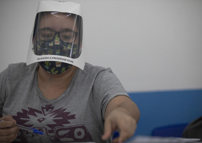 An electoral worker wears a face shield with a sign that reads "I help to preserve lives" during municipal elections at a polling station in the Rocinha slum in Rio de Janeiro, Brazil, Sunday, Nov. 15, 2020. (AP Photo/Silvia Izquierdo)