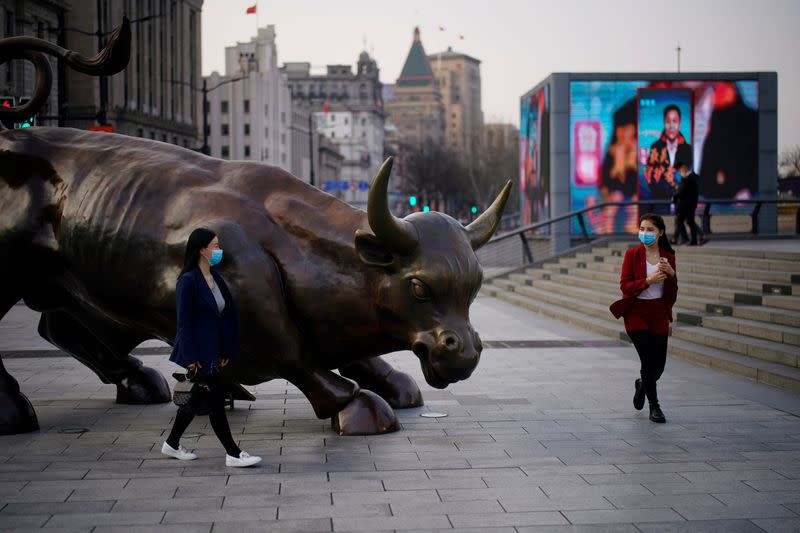 Pedestrians wearing face masks walk near the Bund Financial Bull statue in Shanghai