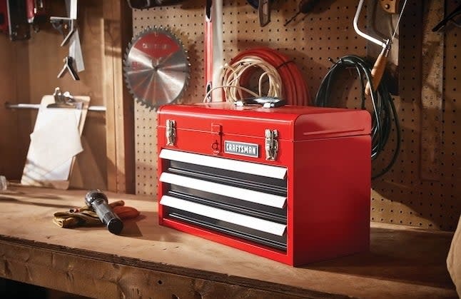A red steel toolbox on a work bench with tools
