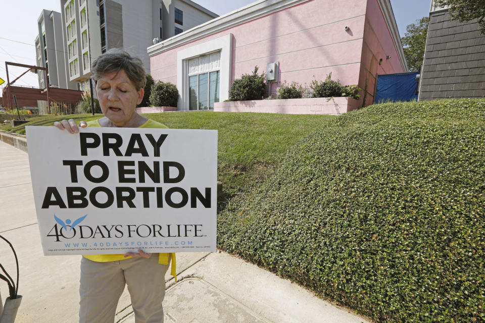 FILE - In this Oct. 2, 2019 file photo, an abortion opponent sings to herself outside the Jackson Womens Health Organization clinic in Jackson, Miss. Three judges from a conservative federal appeals court are hearing arguments, Monday, Oct. 7, over a Mississippi law that would ban most abortions after 15 weeks of pregnancy. Republican Gov. Phil Bryant signed the law in 2018, the state’s only abortion clinic immediately sued and U.S. District Judge Carlton Reeves blocked the law from taking effect. (AP Photo/Rogelio V. Solis)