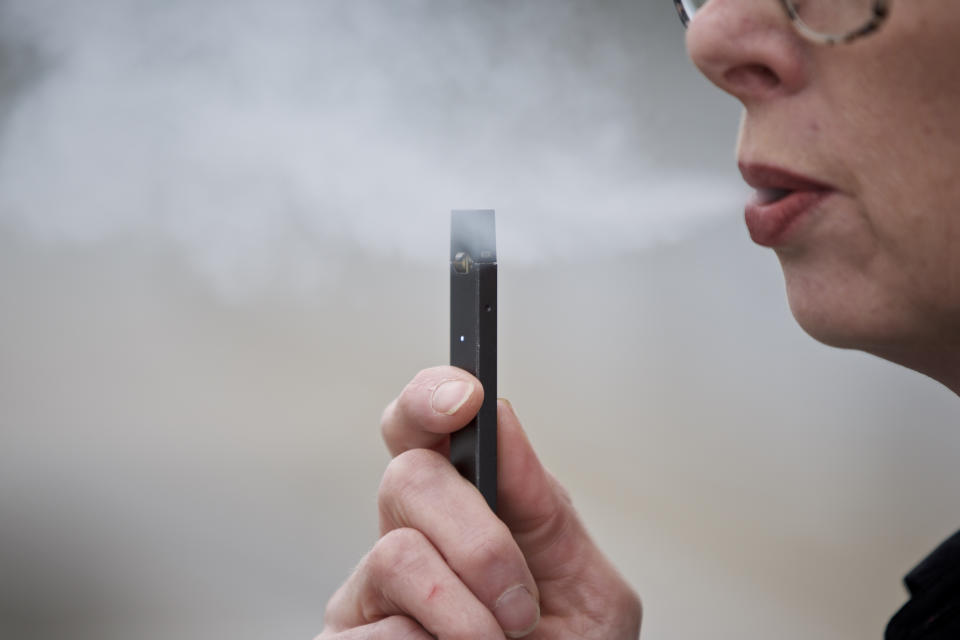 FILE - In this April 16, 2019, file photo, a woman exhales a puff of vapor from a Juul pen in Vancouver, Wash. Juul is the largest U.S. seller of electronic cigarettes, controlling about 70% of the market. The San Francisco-based company rose to the top through viral marketing that promoted high-nicotine pods with dessert and fruit flavors. (AP Photo/Craig Mitchelldyer, File)