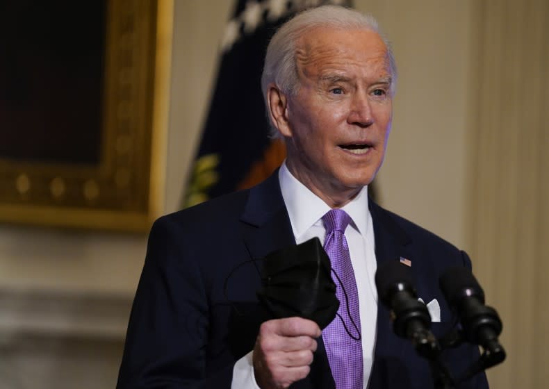 President Joe Biden holds his face mask as he delivers remarks on COVID-19, in the State Dining Room of the White House, Tuesday, Jan. 26, 2021, in Washington. (AP Photo/Evan Vucci)