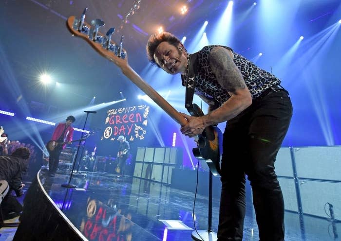 Musician playing guitar on stage with Green Day's logo in the background