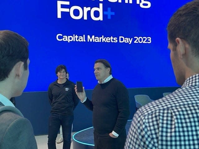Ford CEO Jim Farley holds up his cell phone while talking with automotive industry analysts at the Ford Experience Center in Dearborn on May 22, 2023 after the 8 a.m. to 3 p.m. Capital Markets Day presentations ended. He was making a point about how Americans use technology and the tie between software and revenue at Ford Motor Company. Ted Cannis, CEO of the Ford Pro business unit, looks on as Farley speaks.