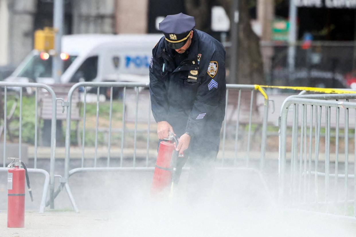 <span>A police officer uses a fire extinguisher as emergency personnel respond to a report of a person covered in flames outside court in New York on Friday.</span><span>Photograph: Brendan McDermid/Reuters</span>