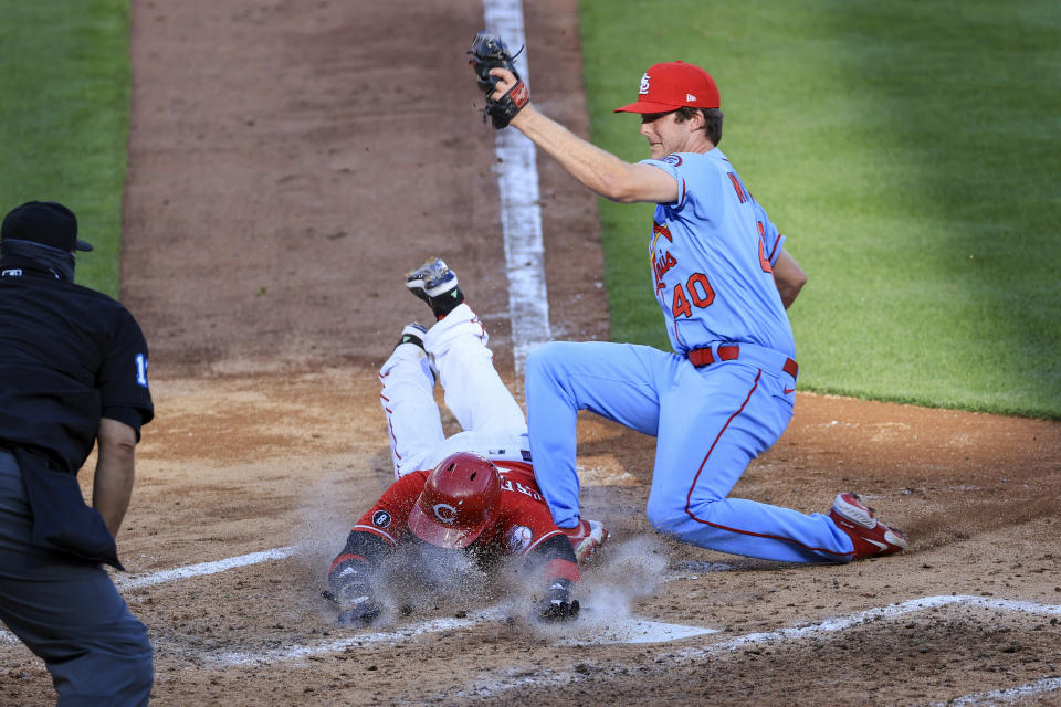 Cincinnati Reds' Nick Castellanos, center, scores a run ahead of the tag by St. Louis Cardinals' Jake Woodford, right, during the fourth inning of a baseball game in Cincinnati, Saturday, April 3, 2021. (AP Photo/Aaron Doster)