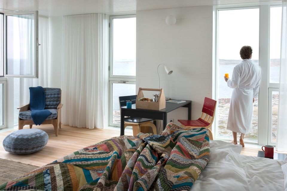 A woman in a bath robe looking out the window of her Fogo Island suite