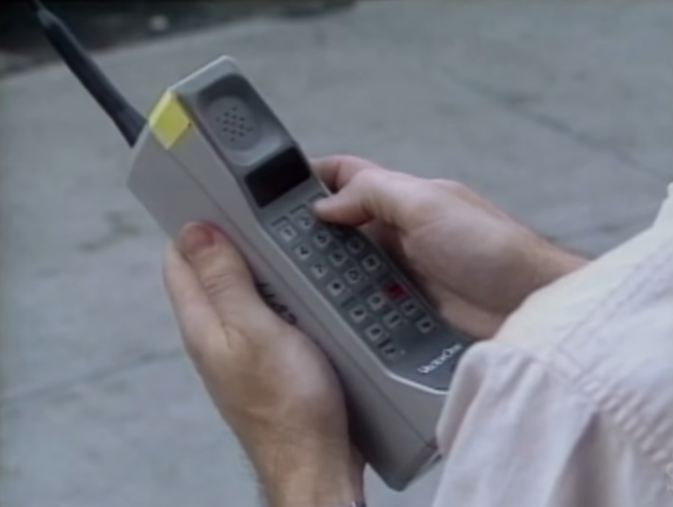 Person holds a large, vintage mobile phone, demonstrating outdated technology in relation to work and connectivity