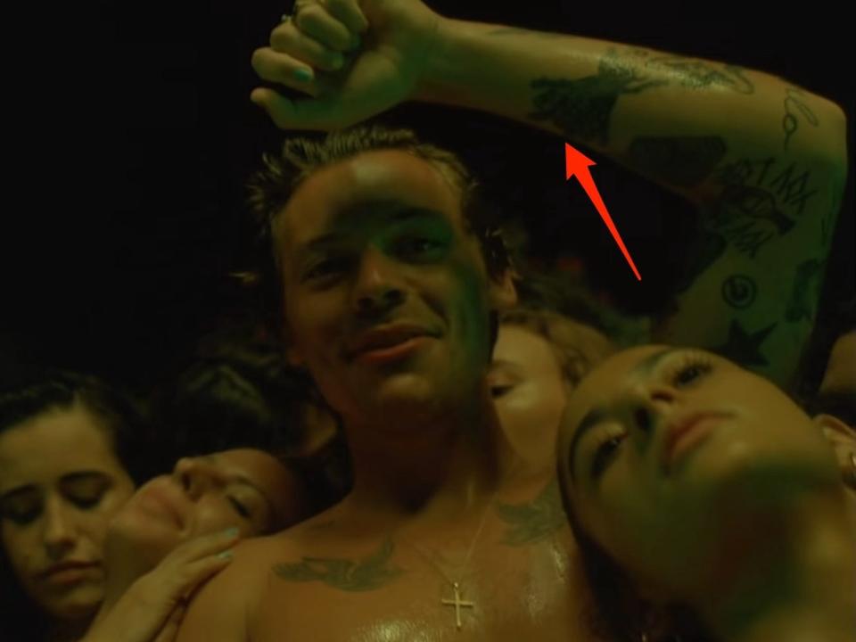 A red arrow pointing to an insect tattoo on Harry Styles' left arm, seen in the music video for "Lights Up."