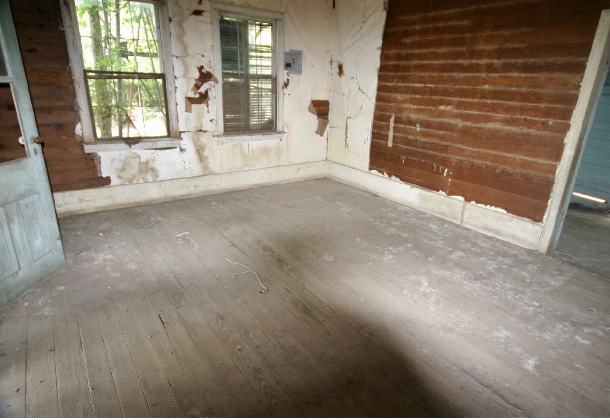 a rundown room with a wood floor and windows