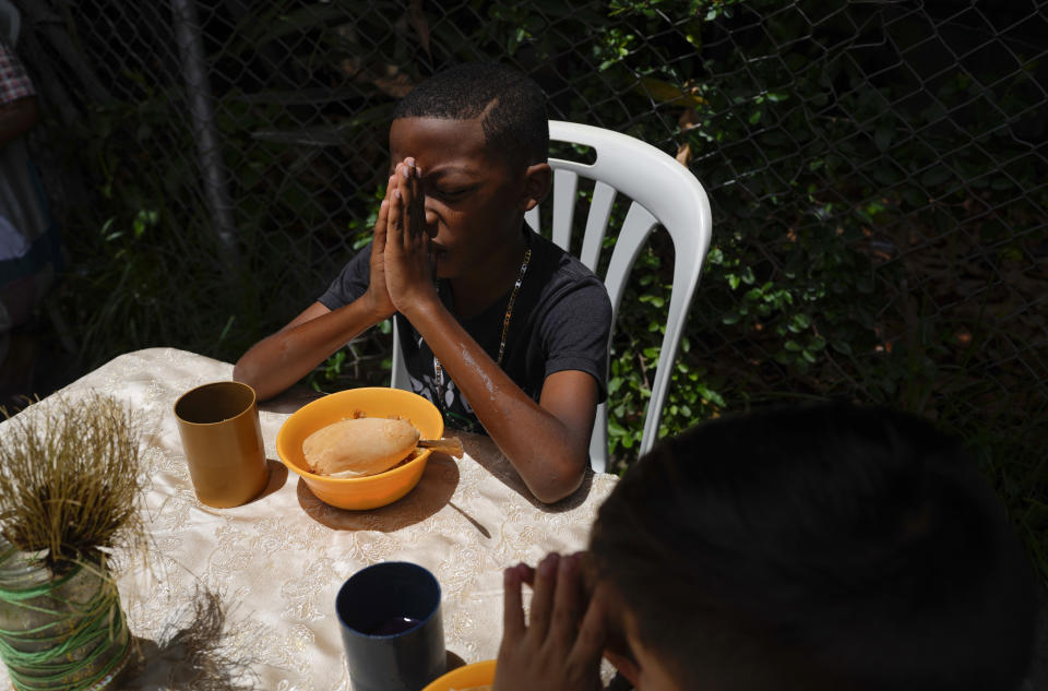 Boys say a prayer before digging into their free lunch donated by the New Birth's Christian church, in the Catia neighborhood of Caracas, Venezuela, Wednesday, June 8, 2022. Once a week, the church hands out over 100 free lunches to low-income children, pregnant women and the elderly. (AP Photo/Ariana Cubillos)