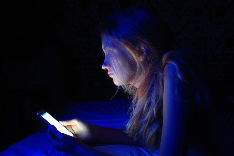 Frau benutzt ihr Smartphone im Dunkeln im Bett