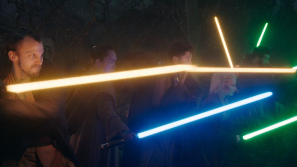  People in robes swing colorful laser swords at one another. 