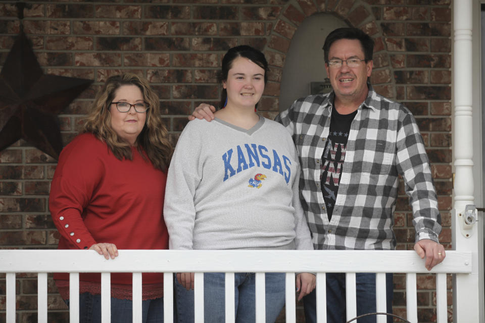 Anna Elskamp, left, and her husband, Rick, right, stand with their oldest daughter, Sheridan, on the front porch of their home, Saturday, Jan. 27, 2024, outside Topeka, Kan. The state recently told the family that Sheridan, now 21, would receive intellectual disability services after she spent 10 years on a waiting list. (AP Photo/John Hanna)
