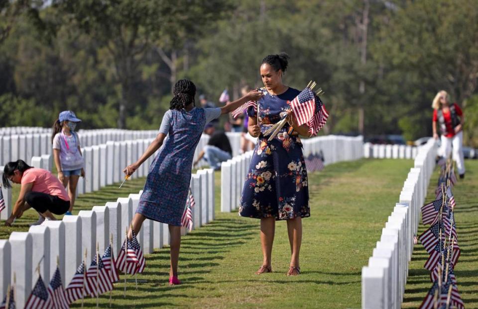 Volunteer Anneka Howell holds American flags as her daughter Adrianna Howell places flags in front of veterans’ headstones at the South Florida National Cemetery.