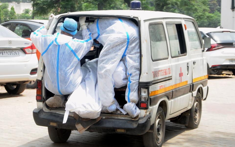 Health workers wearing PPE kits carry the body of a COVID-19 victim from a mortuary for cremation in Patiala on Tuesday.