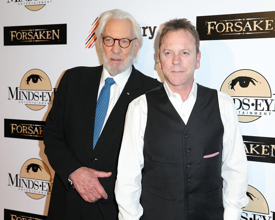 Donald in a suit and tie and Kiefer in a vest and shirt, posing for cameras at a media event